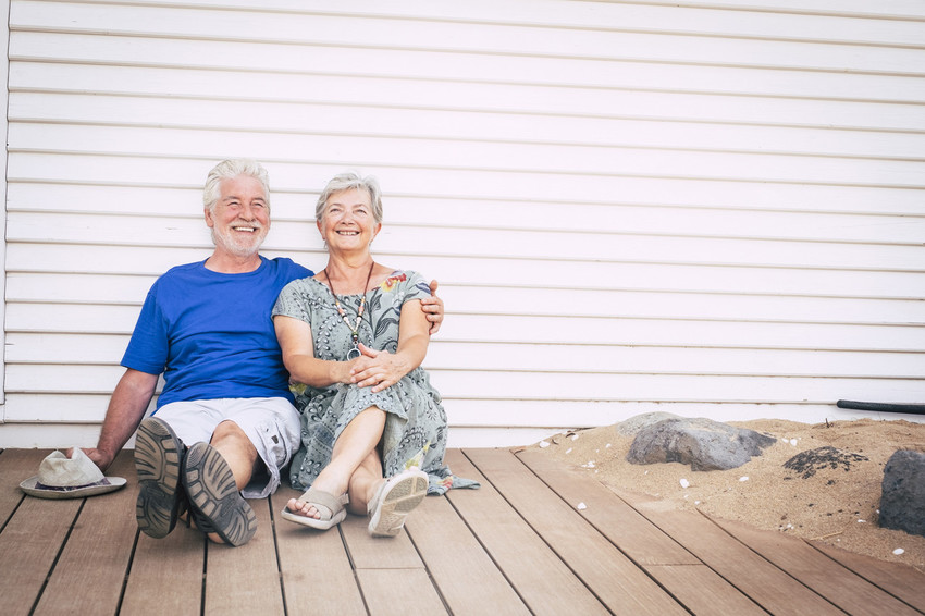 Happy senior couple laughing sitting in the ground on wooden planks on a summer day